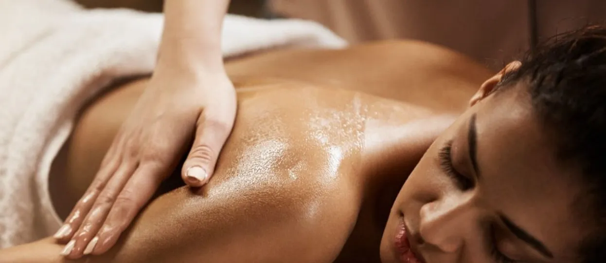 Atendimento de estética corporal na BioDiih Sense: mãos da profissional realizando massagem com óleo nas costas de uma cliente