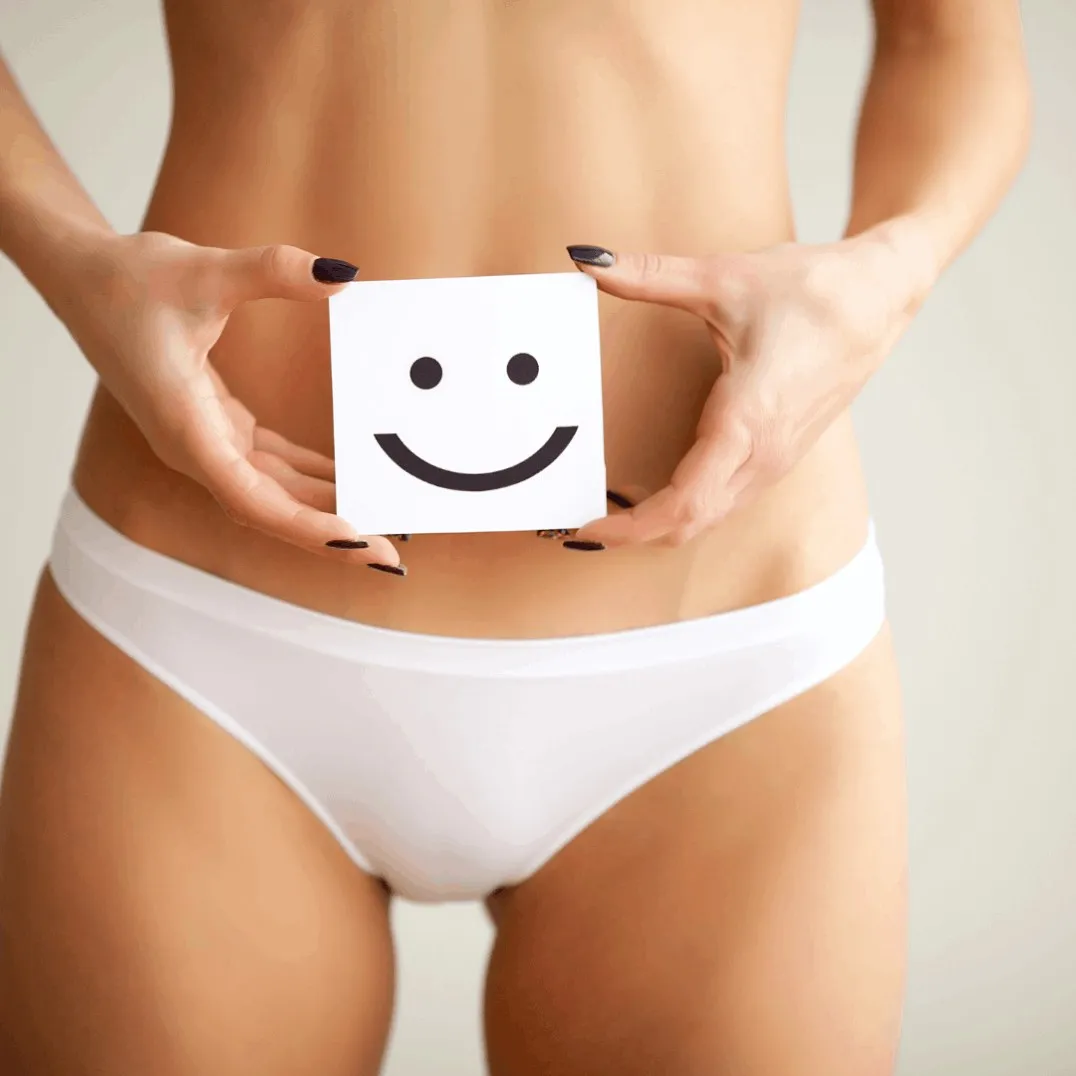 Mulher de roupa íntima branca segurando um cartão com um sorriso desenhado à frente do abdômen, representando bem-estar e autoestima